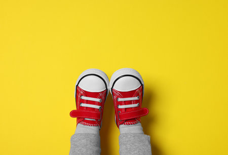 Little child in stylish red gumshoes on yellow background, top viewの写真素材