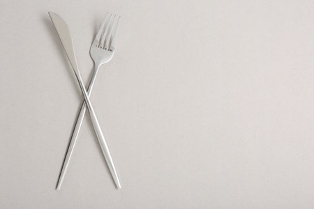 Shiny fork and knife on light gray background, flat lay. Space for textの写真素材