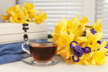 Cup of aromatic tea, beautiful yellow daffodil and iris flowers on windowsillの写真素材