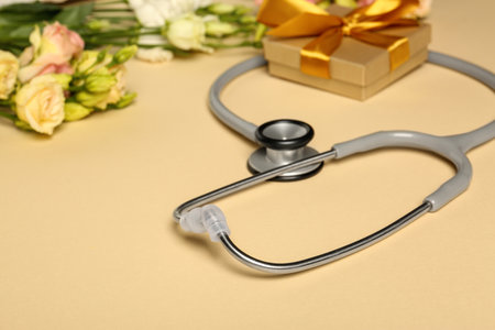 Stethoscope, gift box and eustoma flowers on beige background. Happy Doctor's Dayの写真素材