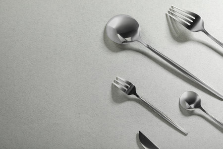 Forks, knife and spoons on gray background, flat lay with space for text. Stylish cutlery set