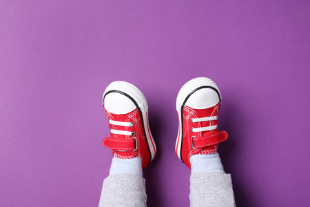 Little child in stylish red gumshoes on purple background, top viewの写真素材