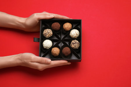 Woman with box of delicious chocolate candies on red background, top viewの写真素材