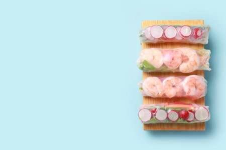 Different delicious spring rolls wrapped in rice paper on light blue background, top view. Space for...
