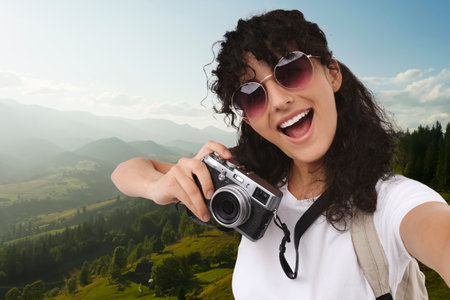 Beautiful woman in sunglasses with camera taking selfie in mountainsの写真素材