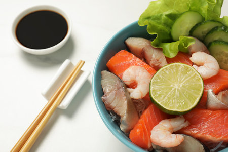 Delicious mackerel, shrimps and salmon served with lettuce, lime, cucumbers and soy sauce on white marble table, closeup. Tasty sashimi dishの写真素材