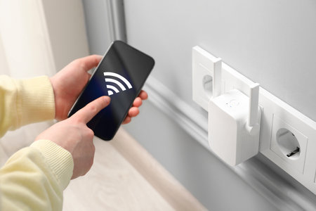 Woman with smartphone connecting to internet via wireless repeater indoors, closeup.