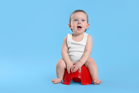 Little child sitting on baby potty against light blue background. Space for textの写真素材