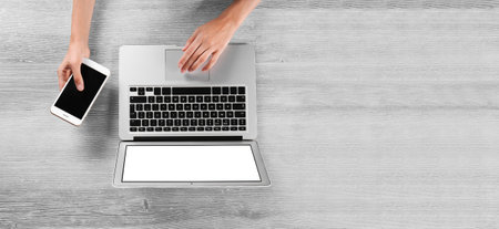 Woman using laptop and mobile phone on white wooden background, top view. Banner design with space for textの写真素材