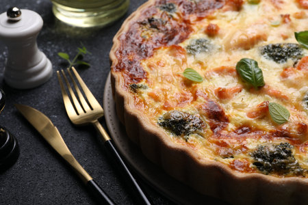 Delicious homemade salmon quiche with broccoli and cutlery on black table, closeupの写真素材