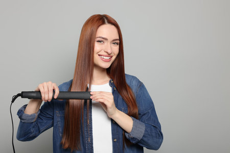 Beautiful woman using hair iron on light gray background, space for textの写真素材