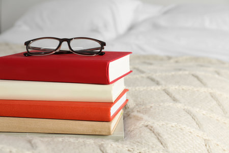 Books and glasses on white soft blanket in bedroom, space for textの写真素材
