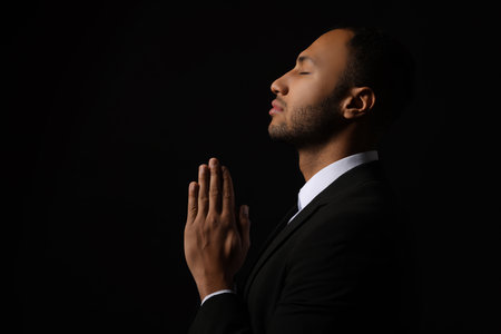 African American man with clasped hands praying to God on black background. Space for textの写真素材
