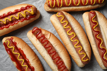 Fresh delicious hot dogs with sauces on parchment paper, flat layの写真素材