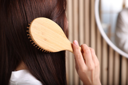 Beautiful woman brushing her hair near mirror in room, closeup. Space for textの写真素材