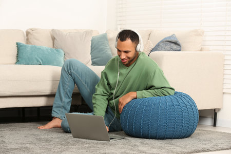 Smiling African American man in headphones with laptop near sofa at homeの写真素材