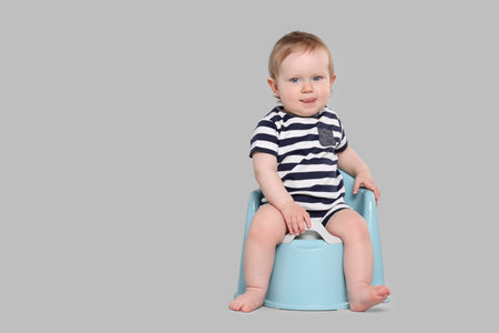 Little child sitting on baby potty against light gray background, space for textの写真素材
