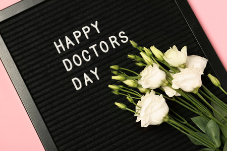 Black letter board with phrase Happy Doctor's Day and beautiful eustoma flowers on pink background, top viewの写真素材