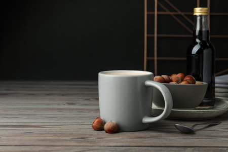 Mug of delicious coffee with hazelnut syrup on wooden table, space for textの写真素材