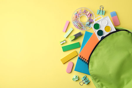 Flat lay composition with different school stationery on pale yellow background, space for text....