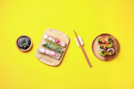 Different delicious spring rolls, chopsticks and soy sauce on yellow background, flat layの写真素材