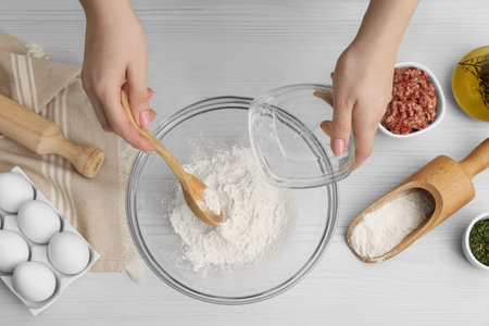 Woman putting flour into bowl at wooden table, top viewの写真素材