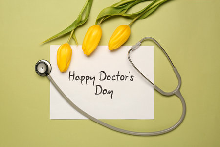Card with phrase Happy Doctor's Day, stethoscope and yellow tulips on light green background, flat layの写真素材