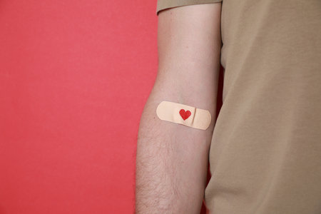 Blood donation concept. Man with adhesive plaster on arm against red background, closeup. Space for textの写真素材