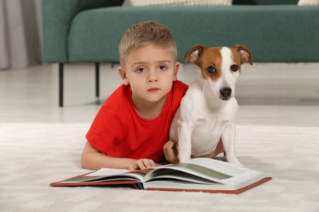 Little boy with book and his cute dog on floor at home. Adorable petの写真素材