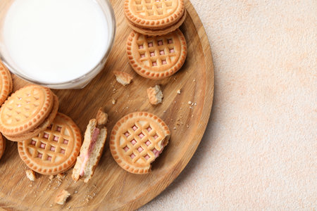 Tasty sandwich cookies with cream and glass of milk on beige background, top view. Space for textの写真素材