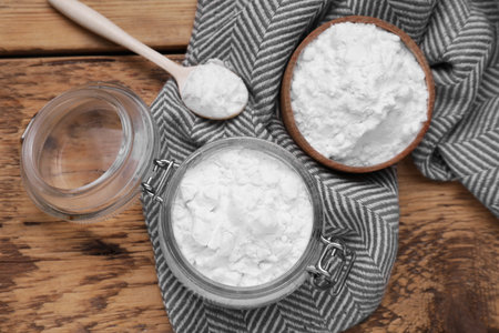 Bowl, spoon and glass jar of natural starch on wooden table, flat lay