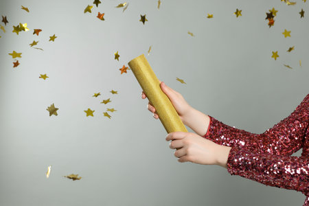 Young woman blowing up party popper on light gray background, closeup