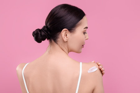 Beautiful woman with smear of body cream on her shoulder against pink background, back viewの写真素材