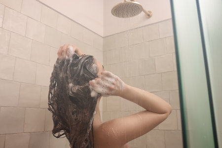 Young woman washing hair while taking shower at homeの写真素材