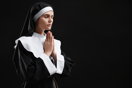 Nun with clasped hands praying to God on black background. Space for textの写真素材