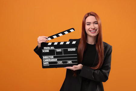 Happy actress with clapperboard on orange background. Film industryの写真素材
