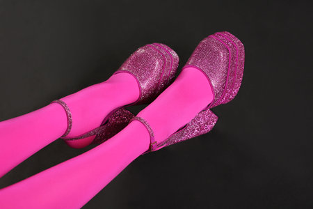 Woman wearing pink tights and high heeled shoes with platform and square toys on black background,...