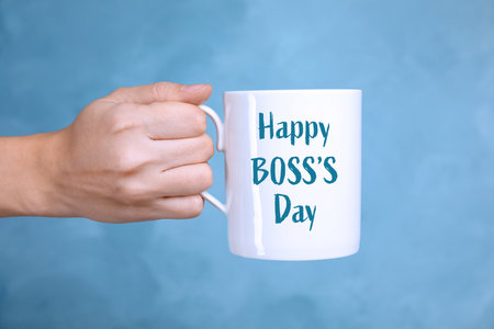 Woman holding mug with phrase Happy Boss`s Day on light blue background, closeupの写真素材