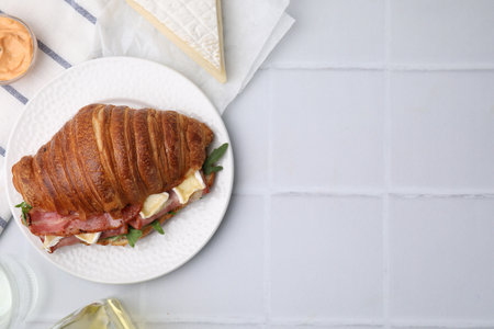 Tasty croissant with brie cheese, ham and bacon on white tiled table, flat lay. Space for textの写真素材