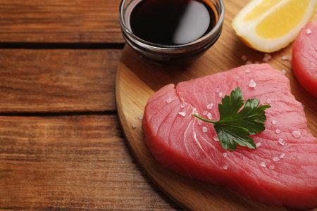 Raw tuna fillet with parsley and spices on wooden table, closeup. Space for textの写真素材