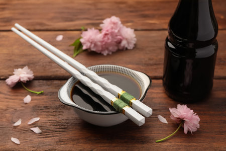 Bottle, bowl with soy sauce, chopsticks and flowers on wooden tableの写真素材
