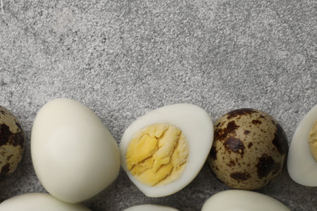 Peeled and unpeeled hard boiled quail eggs on gray table, flat lay. Space for text