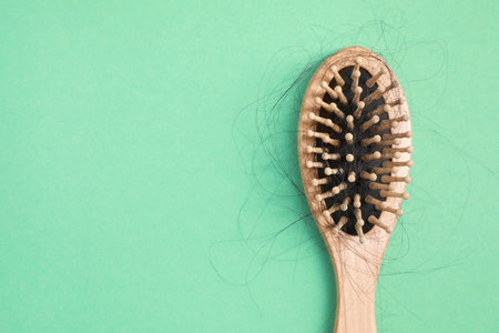 Wooden brush with lost hair on green background, top view. Space for textの写真素材