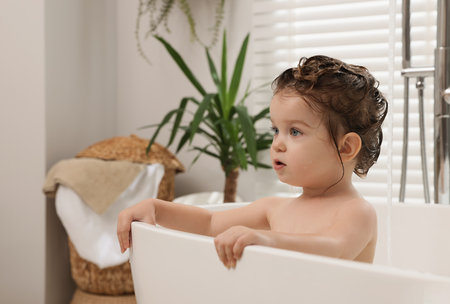 Cute little girl washing hair with shampoo in bathroom