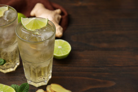 Glasses of tasty ginger ale with ice cubes and ingredients on wooden table, closeup. Space for textの写真素材
