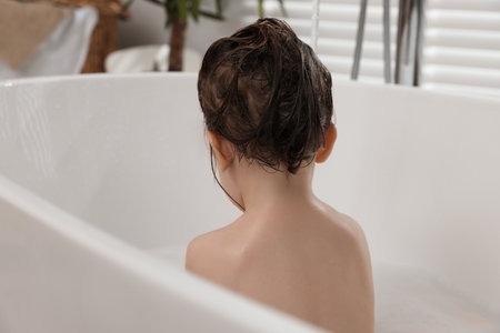 Cute little girl washing hair with shampoo in bathroomの写真素材