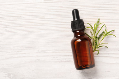 Bottle with essential oil and fresh rosemary on white wooden table, top view. Space for textの写真素材
