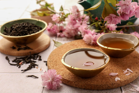 Traditional ceremony. Cup of brewed tea, teapot, dried leaves and sakura flowers on tiled table, closeupの写真素材