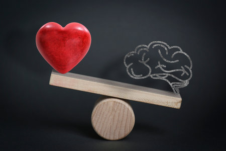 Choosing between logic and emotions. Miniature wooden seesaw with heart and brain against black backgroundの写真素材