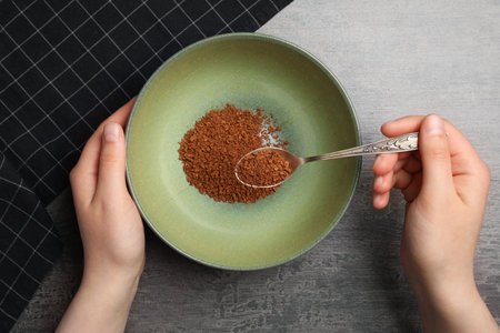 Woman pouring instant coffee granules into bowl at gray table, top viewの写真素材
